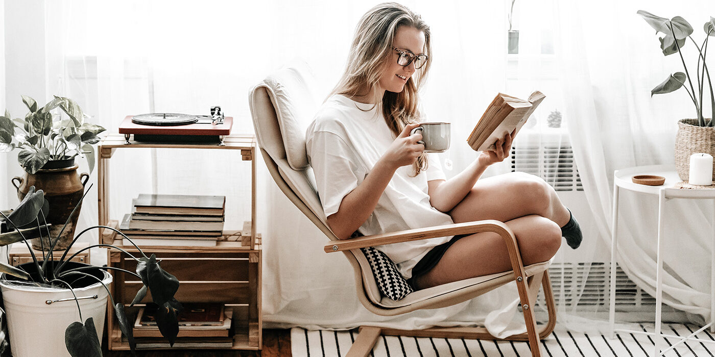 Woman sitting in her apartment reading with a cup of tea